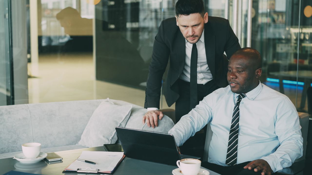Two businessmen collaborating in a modern office, working on a laptop.